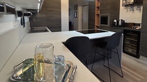 A modern kitchen with a dining area, featuring a tray with glasses and a bottle, a built-in oven, and a coffee machine. - LAKEHOUSE ENJOY (Pallanza)