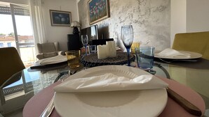 A dining table set with plates, cutlery, and glasses, with a painting and a television in the background. - LAKEHOUSE ENJOY (Pallanza)
