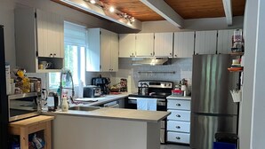 Een moderne keuken met witte kastjes, een centraal eiland, roestvrijstalen apparatuur en een houten plafond.