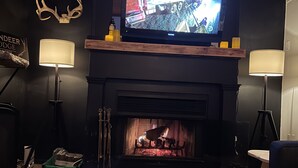 Een gezellige woonkamer met een open haard, een televisie erboven en een bord op de muur.