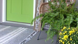 Une porte verte, une chaise en osier, une petite table ornée de fleurs jaunes et une citrouille sur le porche.