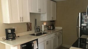 A compact kitchen with white cabinets, a dishwasher, a coffee maker, and a refrigerator.