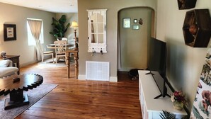 A cozy living room with wooden flooring, a round table, a sofa, and a TV on a stand.