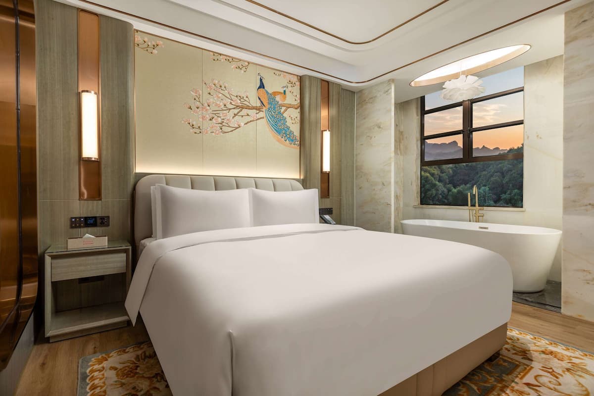 Quarto de hotel moderno com uma cama grande, uma banheira e vista para uma floresta pela janela.