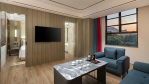 Ein modernes Hotelzimmer mit Flachbildfernseher, einem Marmortisch, einer Sitzecke und einem großen Fenster mit Blick ins Freie.