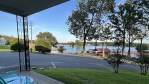A covered outdoor seating area with metal chairs and a view of a lake and buildings in the background. - Peacefull Lake Get-Away (Hot Springs)