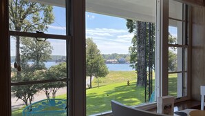 A room with large windows offering a view of a lake, a grassy area, and buildings across the water. - Peacefull Lake Get-Away (Hot Springs)