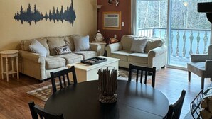 Ein gemütliches Wohnzimmer mit Holzboden, einem Esstisch mit Stühlen, einer Sofagarnitur und einem Bergpanorama an der Wand.