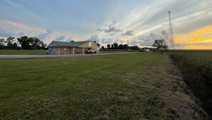 Paisaje rural con una casa, un campo y una torre de transmisión.