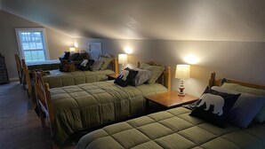 Una habitación con tres camas, cada una con ropa de cama verde y cabeceras de madera. Hay lámparas de noche y una ventana con vistas al exterior.