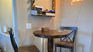 Un comedor con una mesa redonda de madera, dos sillas, un espejo con luces y un letrero de neón que dice "Duck Blind Tavern".