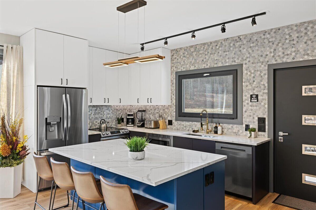 A modern kitchen with white cabinets, a large island with a marble countertop, and a built-in oven.