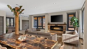 A modern living room with a wooden dining table, sofas, a fireplace, and a large TV.