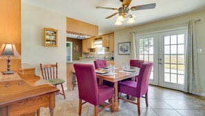 Un coin repas avec une table en bois et des chaises violettes, un ventilateur de plafond et une vue à travers une porte vitrée.