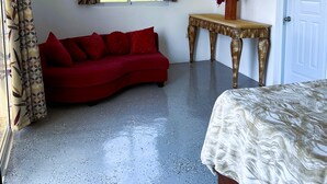 Un dormitorio con un sofá rojo, una mesa de madera con un florero y una cama, y vistas al mar a través de una ventana.