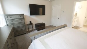 A bedroom with a bed, a dresser, a small table, a television, and a door.