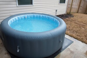 An inflatable hot tub with a blue mosaic tile interior, placed on a concrete pad in front of a house.