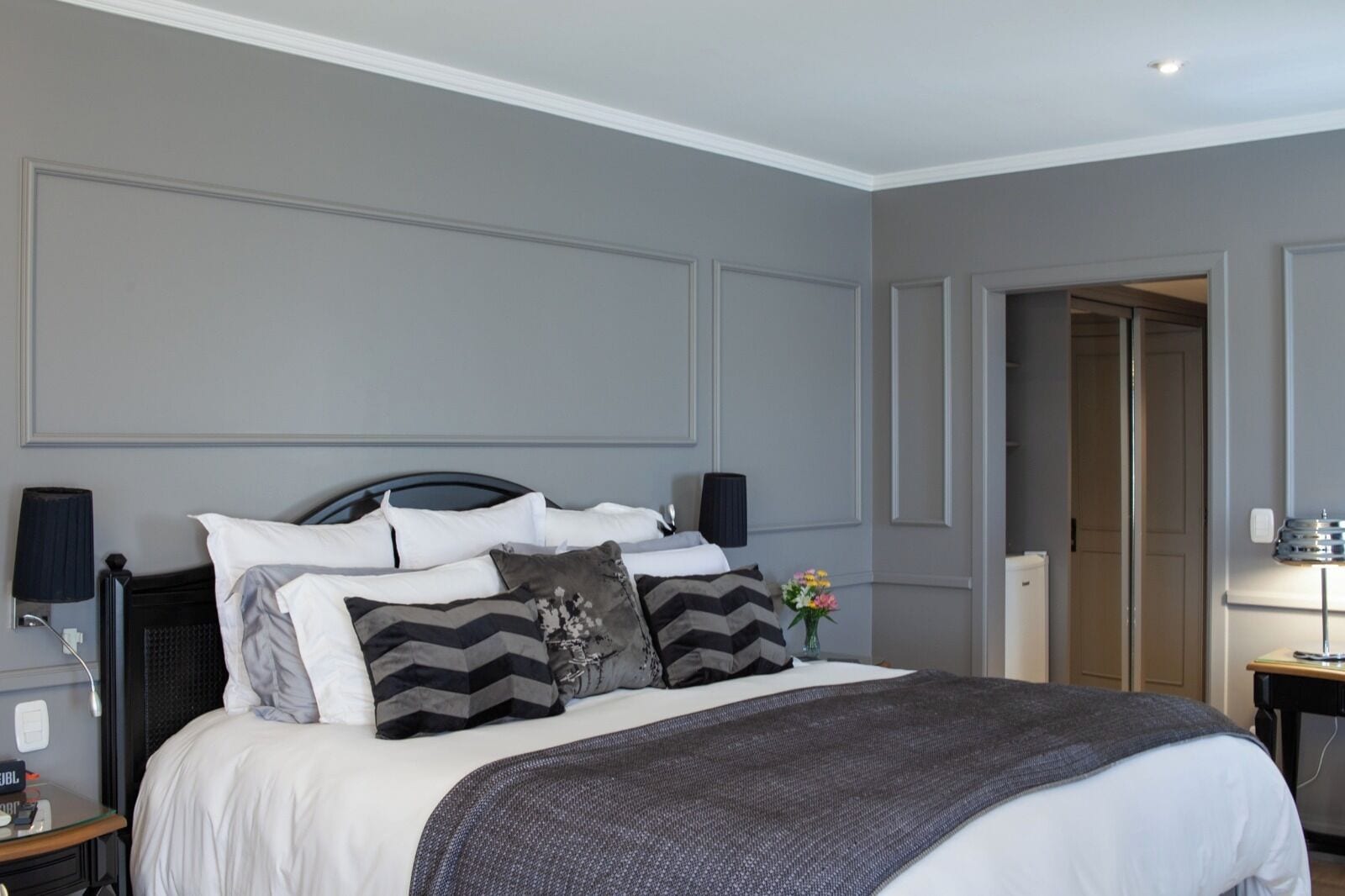 A neatly made bed with a grey blanket, multiple pillows, and a bedside table with a lamp.