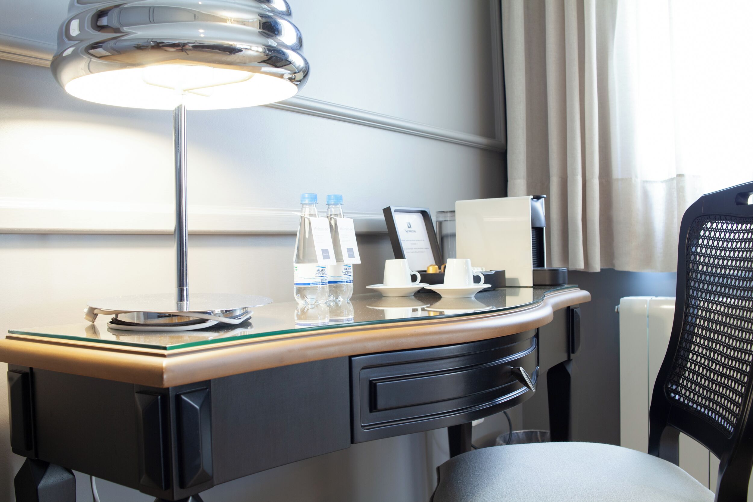 A hotel desk with a lamp, water bottles, a coffee maker, and a phone.