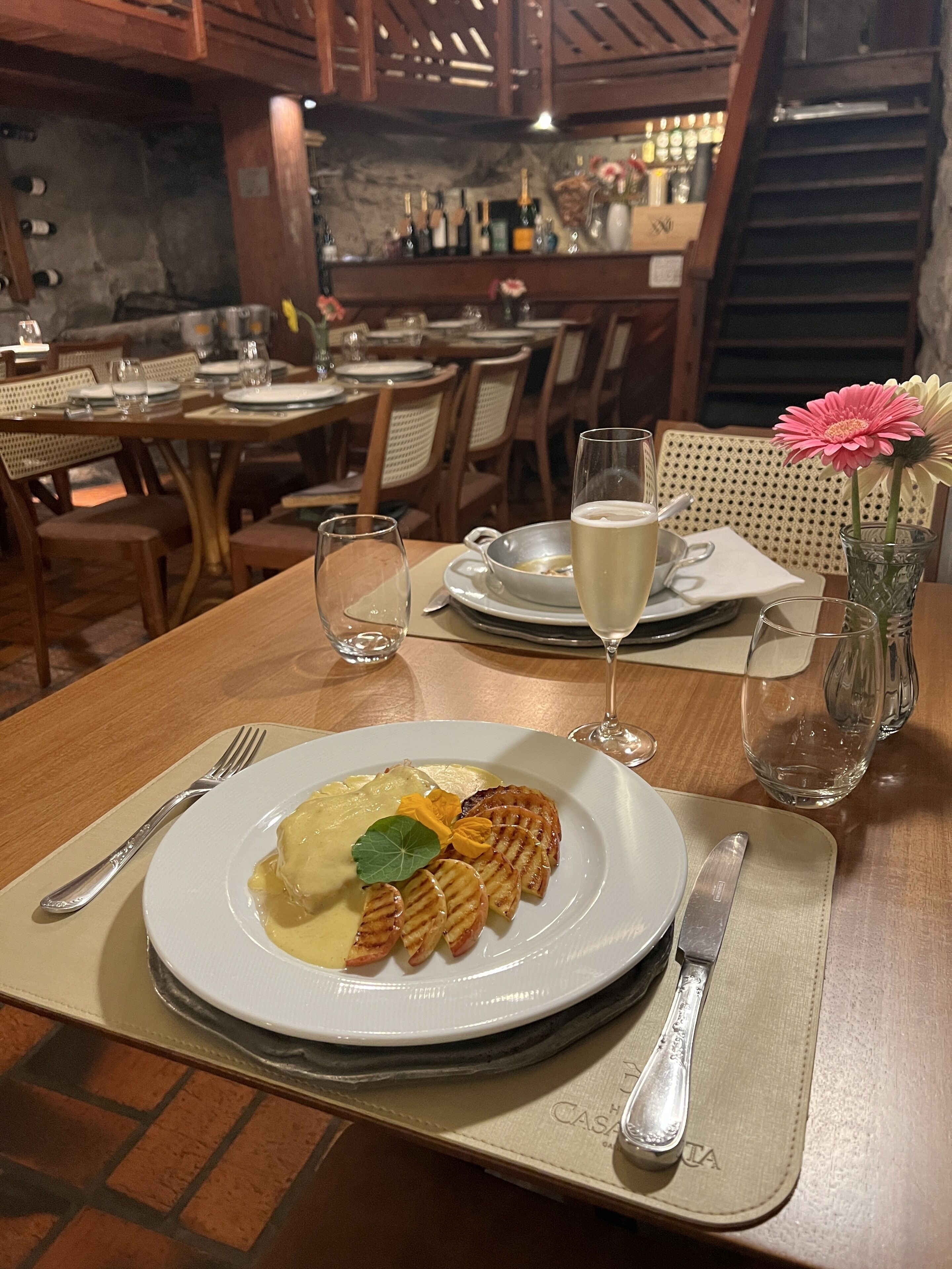 A dining table with a plate of food, a glass of white wine, and a vase with flowers.