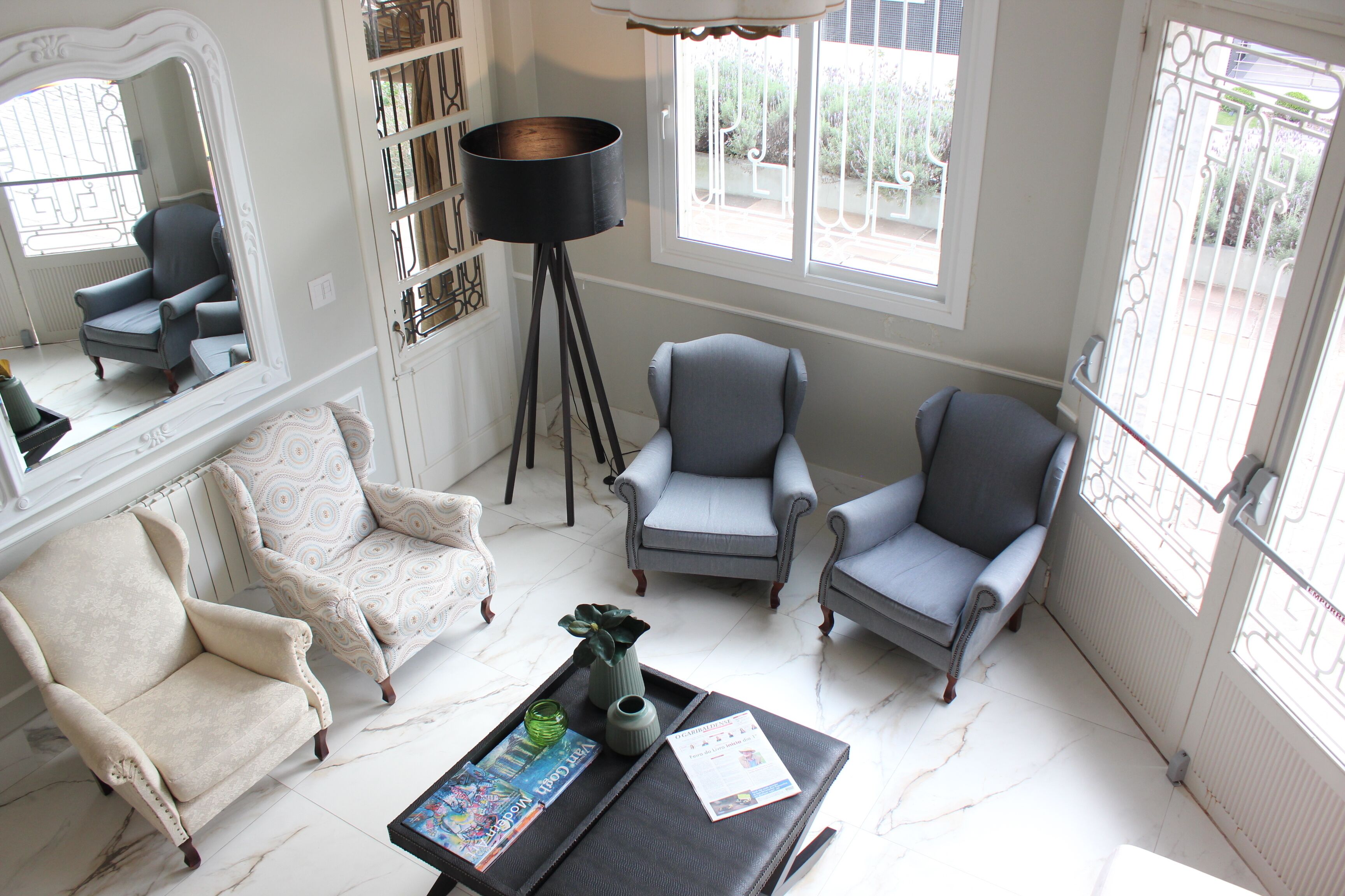 A spacious living room with a large mirror, two armchairs, a coffee table with magazines, and a floor lamp.