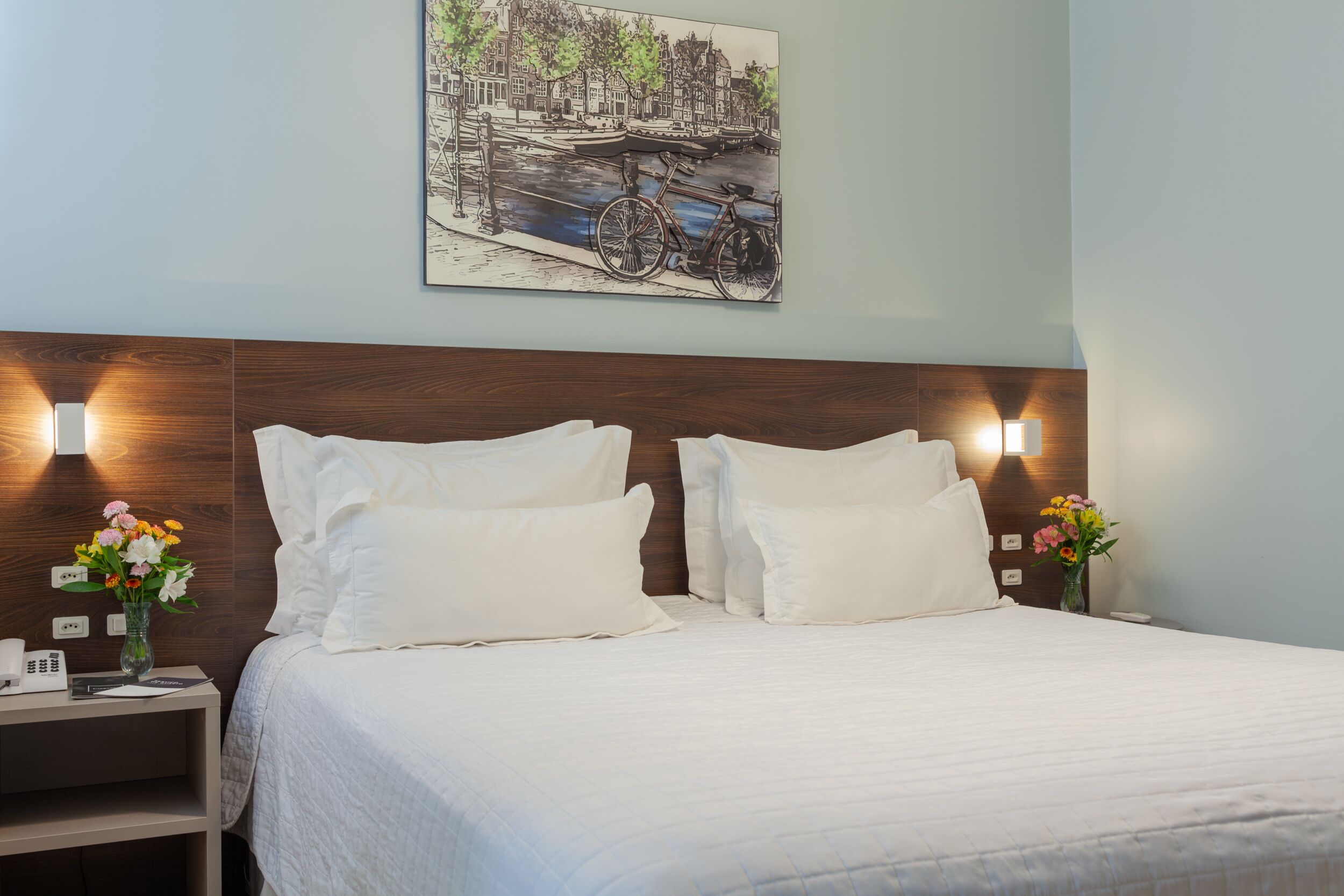 A neatly made bed with white linens, a wooden headboard, and two bedside tables with lamps.