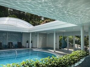 A modern indoor pool with a glass ceiling, lounge chairs, and potted plants. - Hotel Casacurta (Garibaldi)