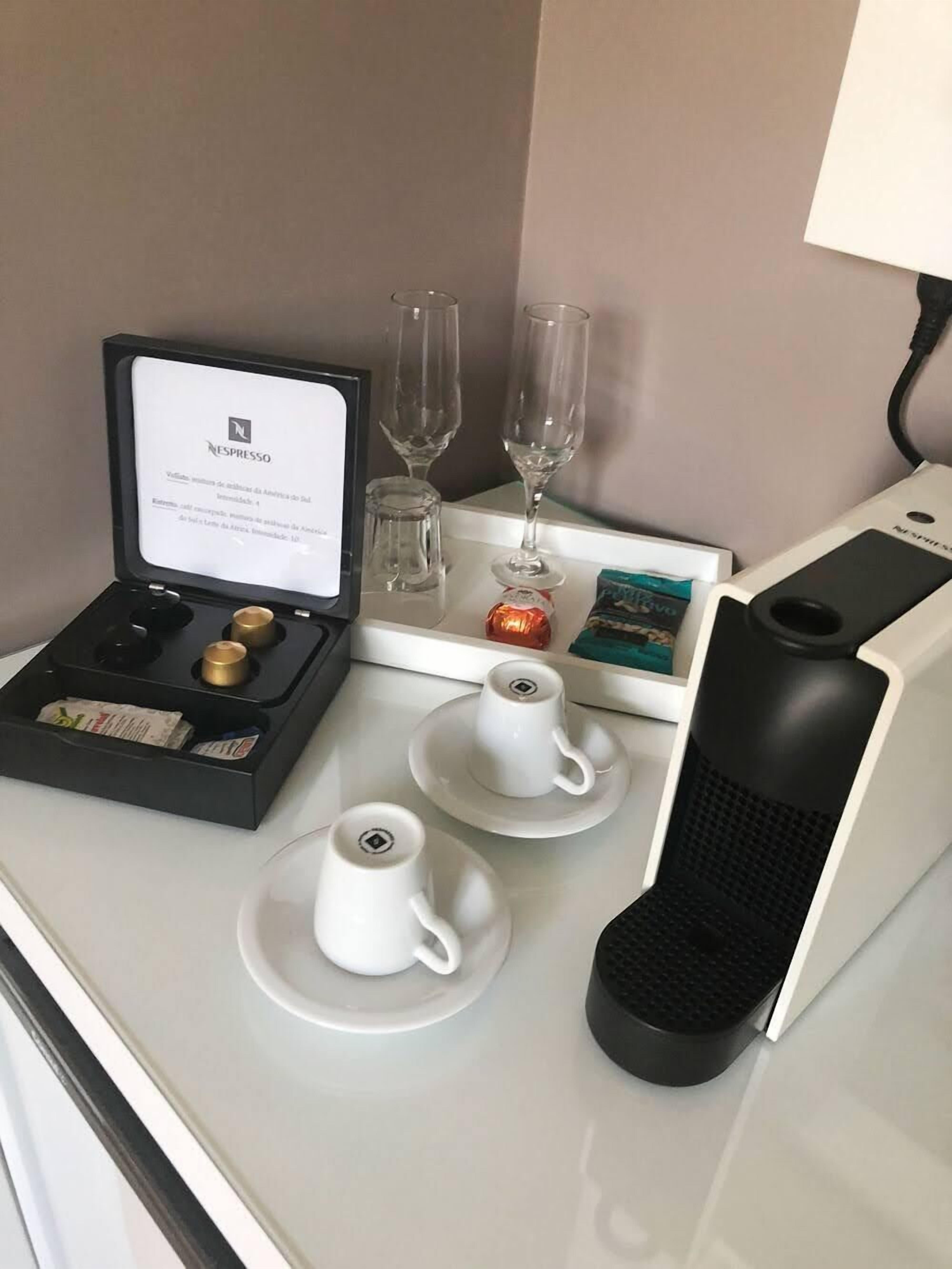 A neatly arranged coffee station with a Nespresso machine, two cups, two glasses, a small box of coffee pods, and a decorative item.