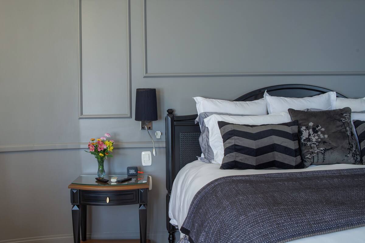 A neatly arranged bedroom with a bed, bedside table, lamp, and a vase with flowers.