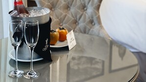 Habitación de hotel con una cama, un cabecero acolchado, una mesa con una botella de champán, dos copas y un plato con fruta.