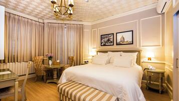 Habitación de hotel con una cama grande, un escritorio, una silla, una mesita con un florero y un banco.