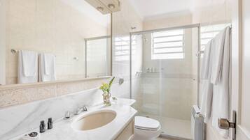 A modern bathroom with a marble sink, a glass shower enclosure, and a toilet.