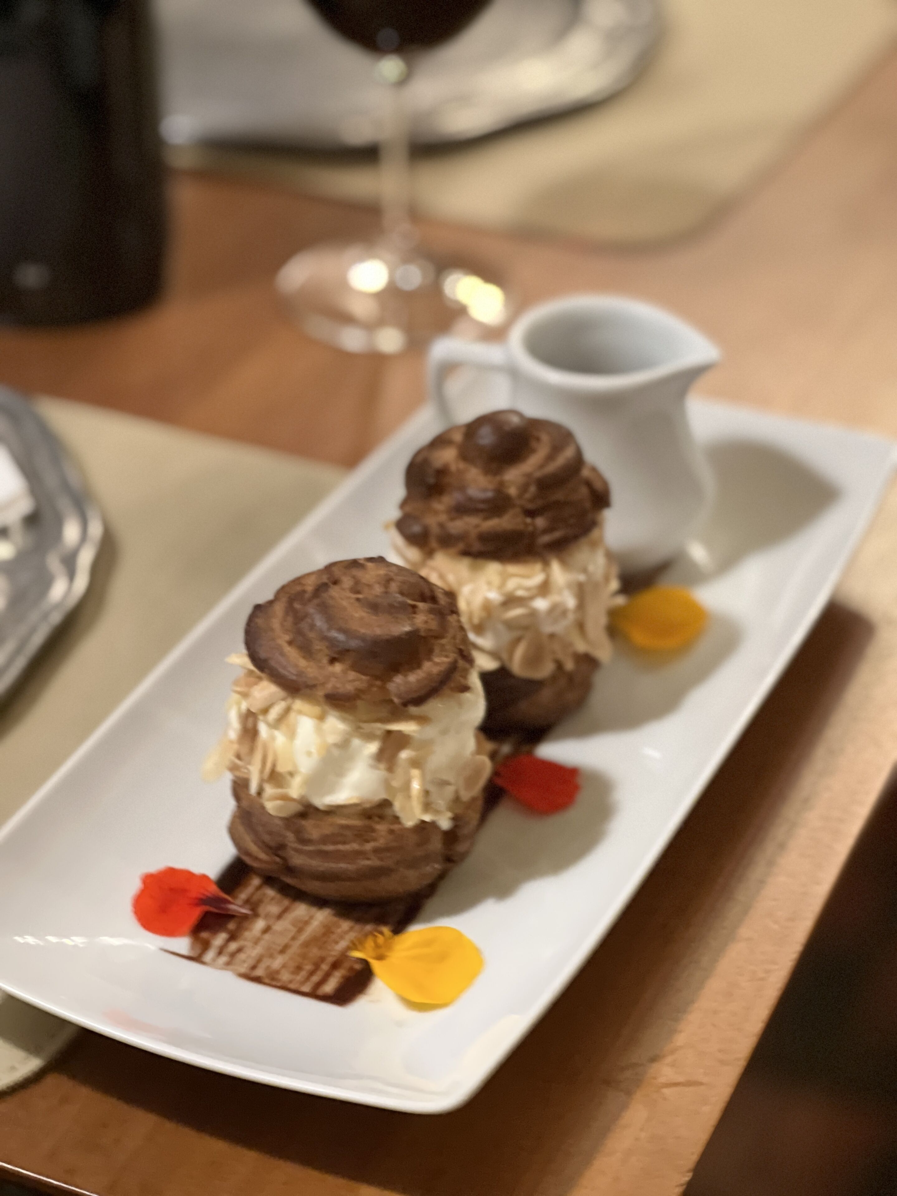 Un plato de postre con dos merengues de chocolate y una pequeña jarra de crema.