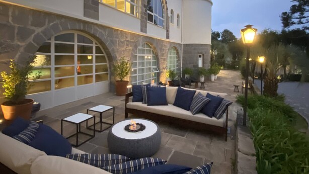 Un patio al aire libre con una chimenea de piedra, un conjunto de sofás y una mesa de comedor.