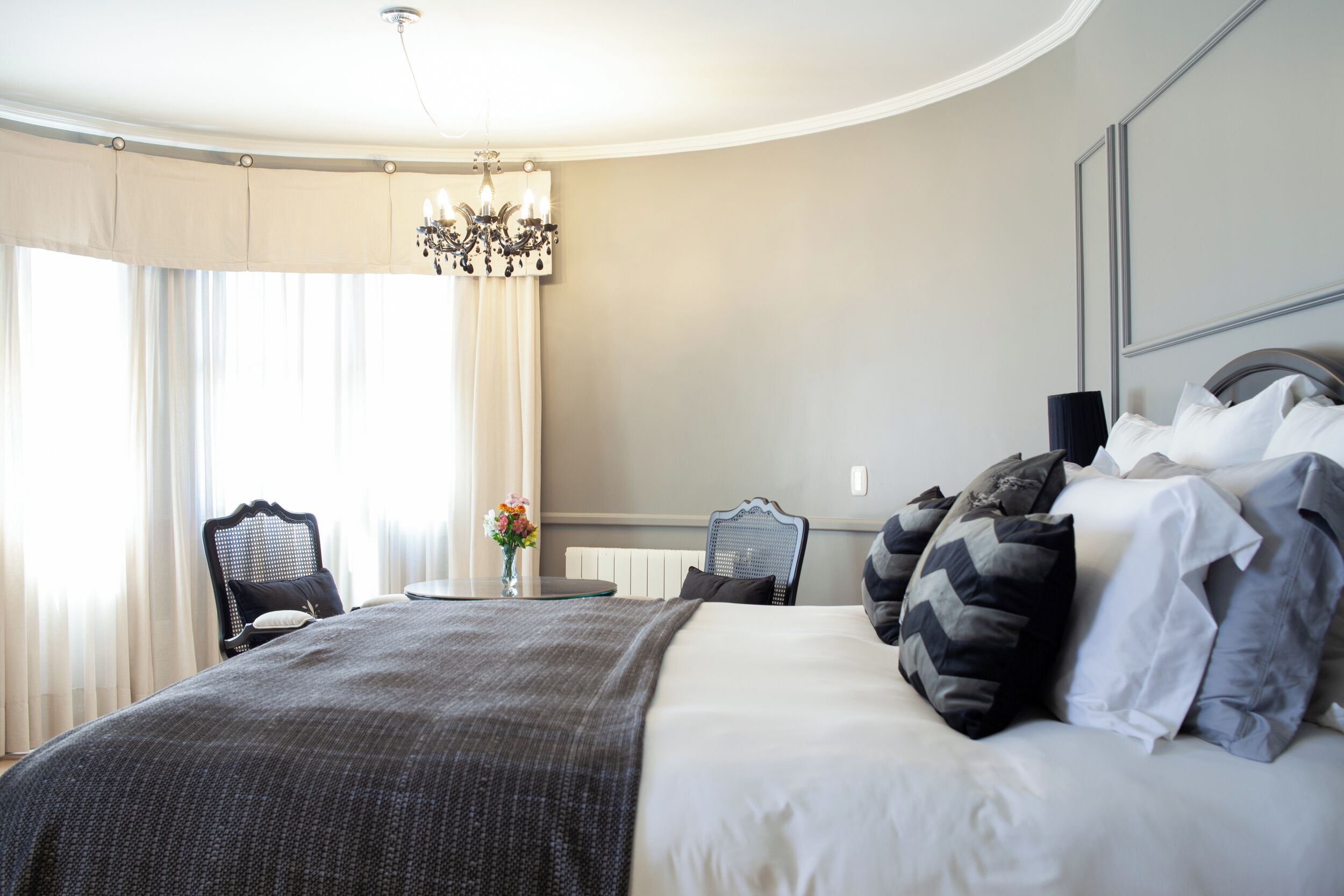Habitación de hotel con una cama grande, un candelabro, una mesa de comedor con sillas y vistas al exterior.
