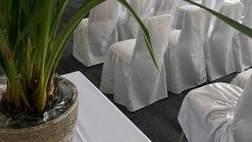 Habitació d'hotel amb una finestra gran, una planta en test amb flors grogues i cadires blanques ordenades.