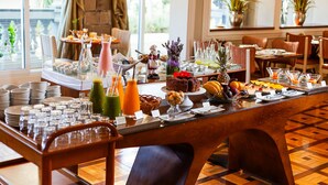 Un bufé de desayuno con diversos alimentos y bebidas, dispuesto en una mesa larga rodeada de sillas.