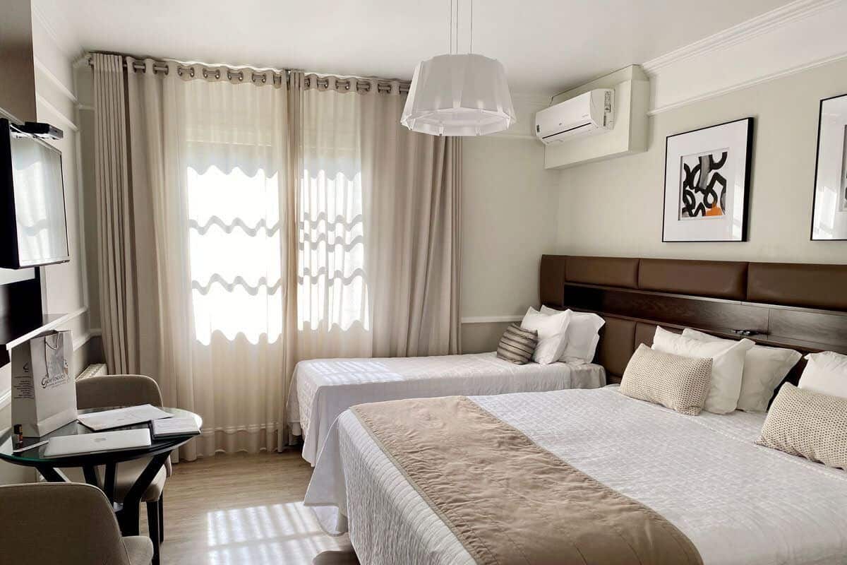 A hotel room with two beds, a desk, a chair, a TV, and a window with curtains.