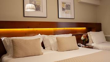 Une chambre d’hôtel avec un grand lit, deux tables de chevet, une petite table et un climatiseur fixé au mur.