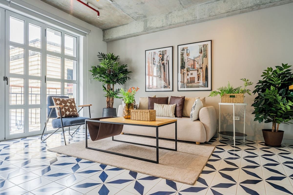 Un salon moderne avec un canapé, une table basse et des fauteuils. Il y a deux grandes fenêtres et une porte.