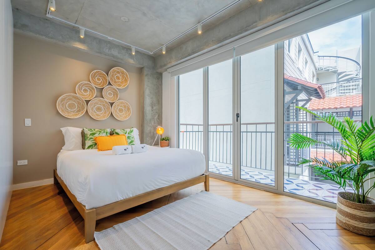 Une chambre moderne avec un grand lit, une vue sur le balcon extérieur et une plante en pot.