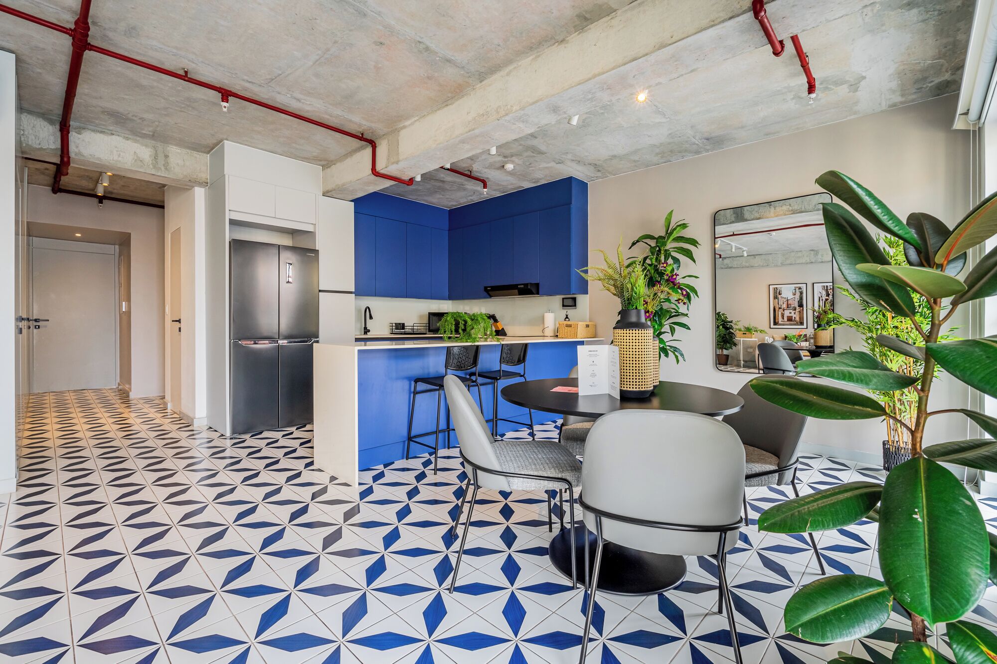A modern kitchen with blue cabinets, a stainless steel refrigerator, and a dining area with a round table and chairs.