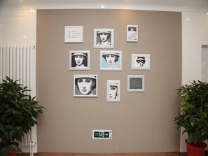 Una pared con varios cuadros enmarcados, un radiador y plantas en macetas.