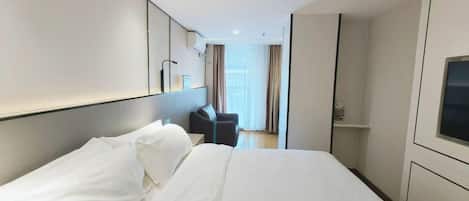 A hotel room with a large bed, a desk, a chair, and a TV.