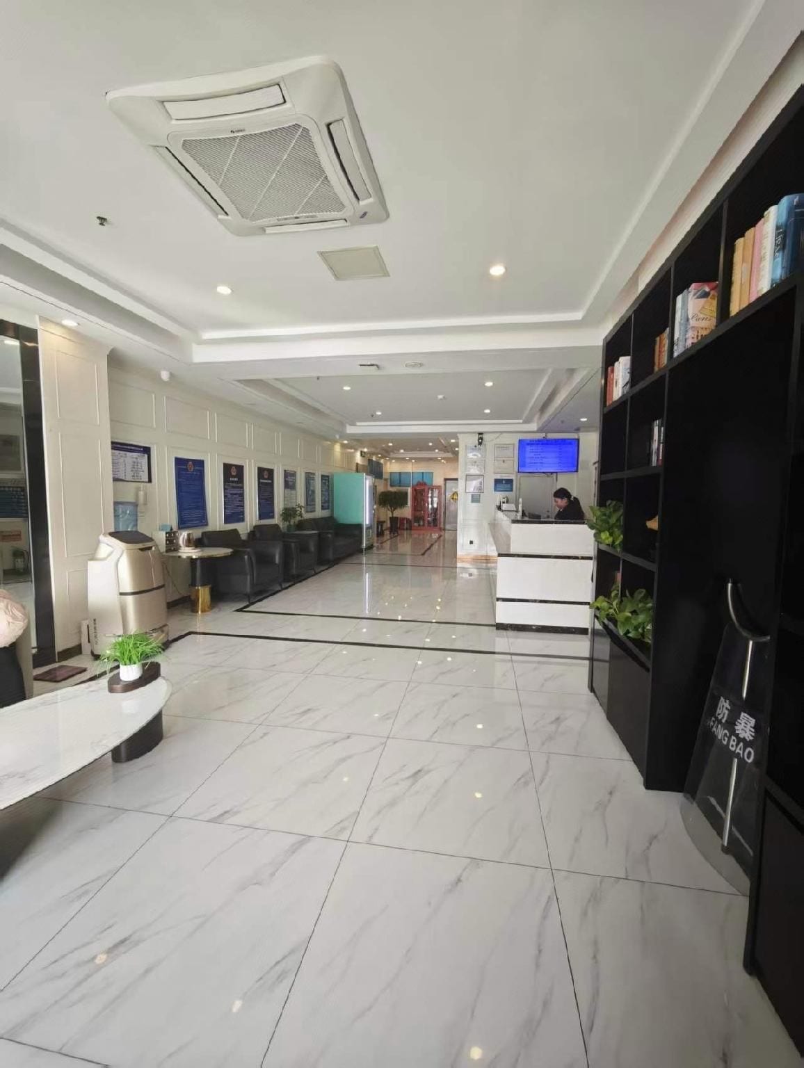 A hotel lobby with a reception desk, seating area, and a bookshelf.
