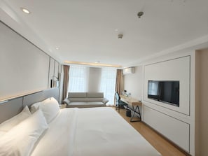 Een hotelkamer met een groot bed, een bureau met stoel, een televisie en een raam met gordijnen.