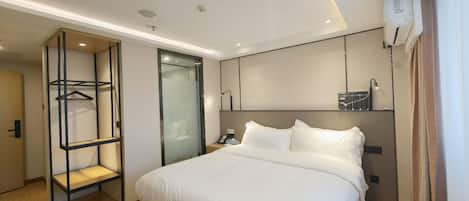A modern hotel room with a large bed, a built-in wardrobe, a bedside table, and a wall-mounted air conditioning unit.