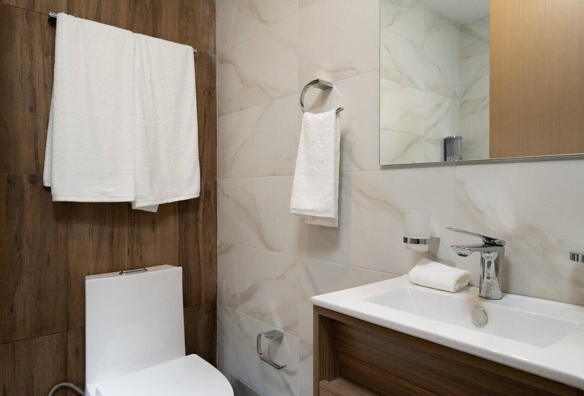 Ein modernes Badezimmer mit einem Holzbadschränkchen, einem weißen Waschbecken und einem Spiegel.