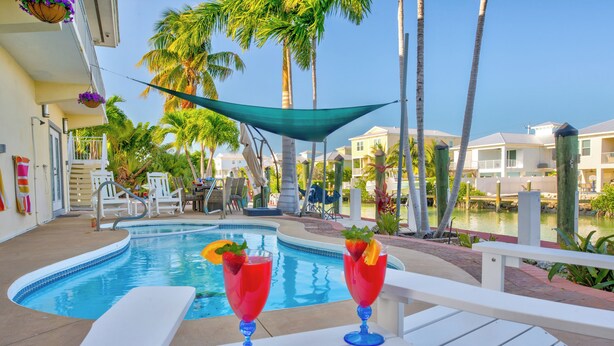 A poolside area with lounge chairs, a pool, and a view of a residential area with palm trees. - Sunchasers Paradise - lux home, private pool/spa, 80' dock (Marathon)