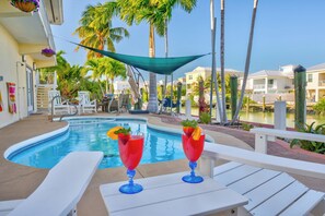 A poolside area with lounge chairs, a pool, and a view of a residential area with palm trees.